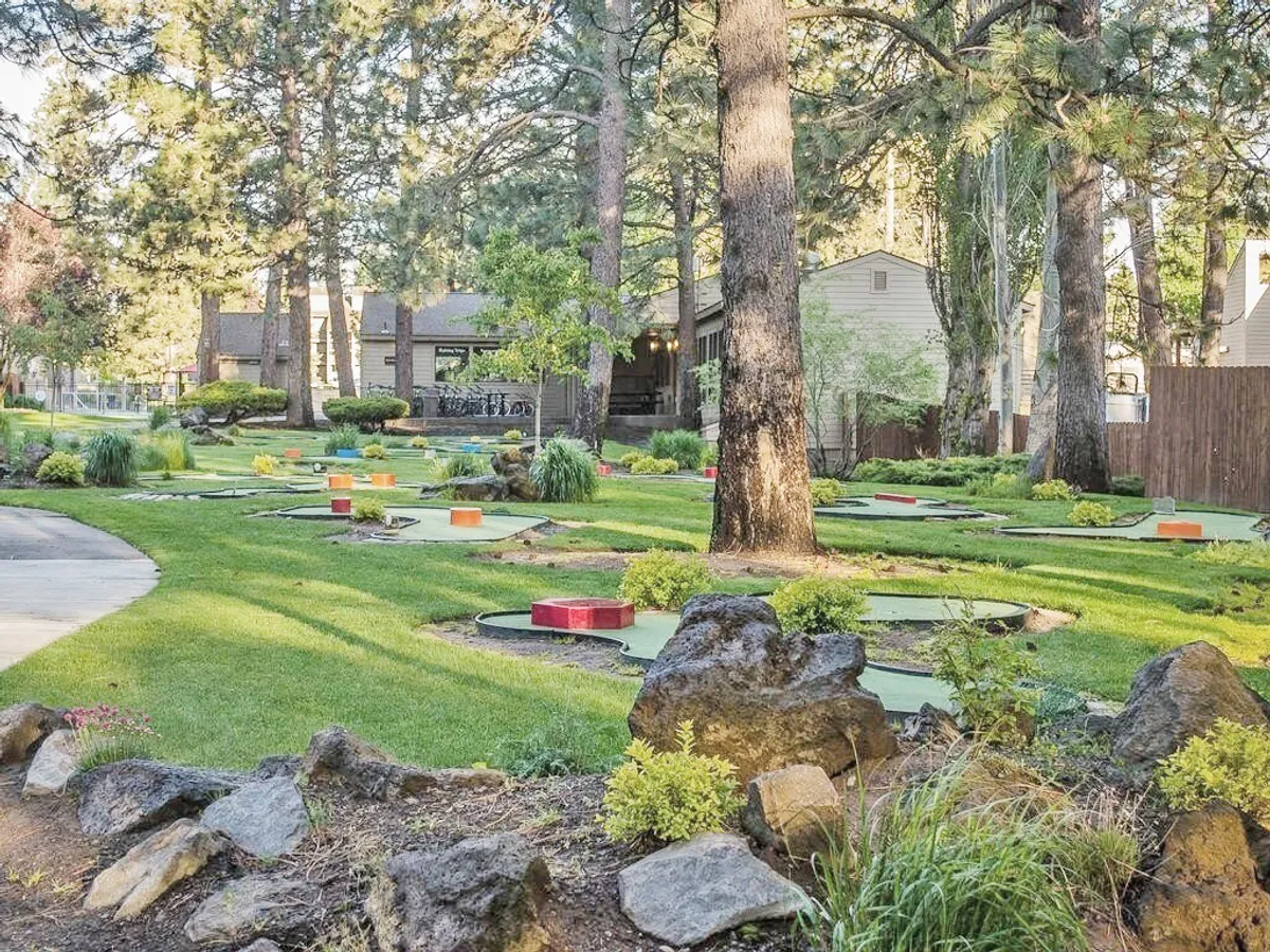 This exterior image captures a well-maintained mini-golf course surrounded by lush greenery and scenic trees, with inviting pathways winding through the space. The setting is bright and cheerful, emphasizing outdoor recreation and relaxation.