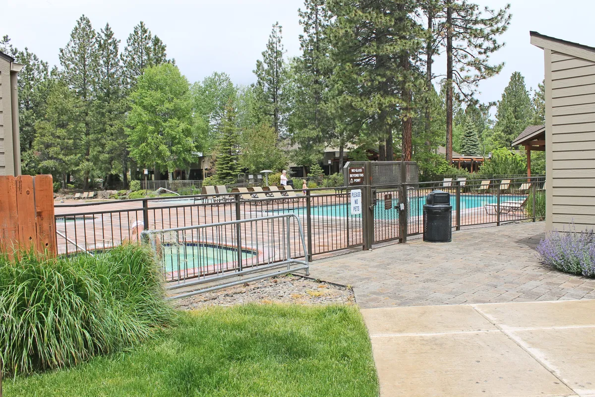 A spacious outdoor swimming pool is at the center of this image, flanked by comfortable lounge chairs and set within a fenced, landscaped area. The surroundings encourage swimming, sunbathing, and socializing, with scenic greenery creating a resort-like feel.