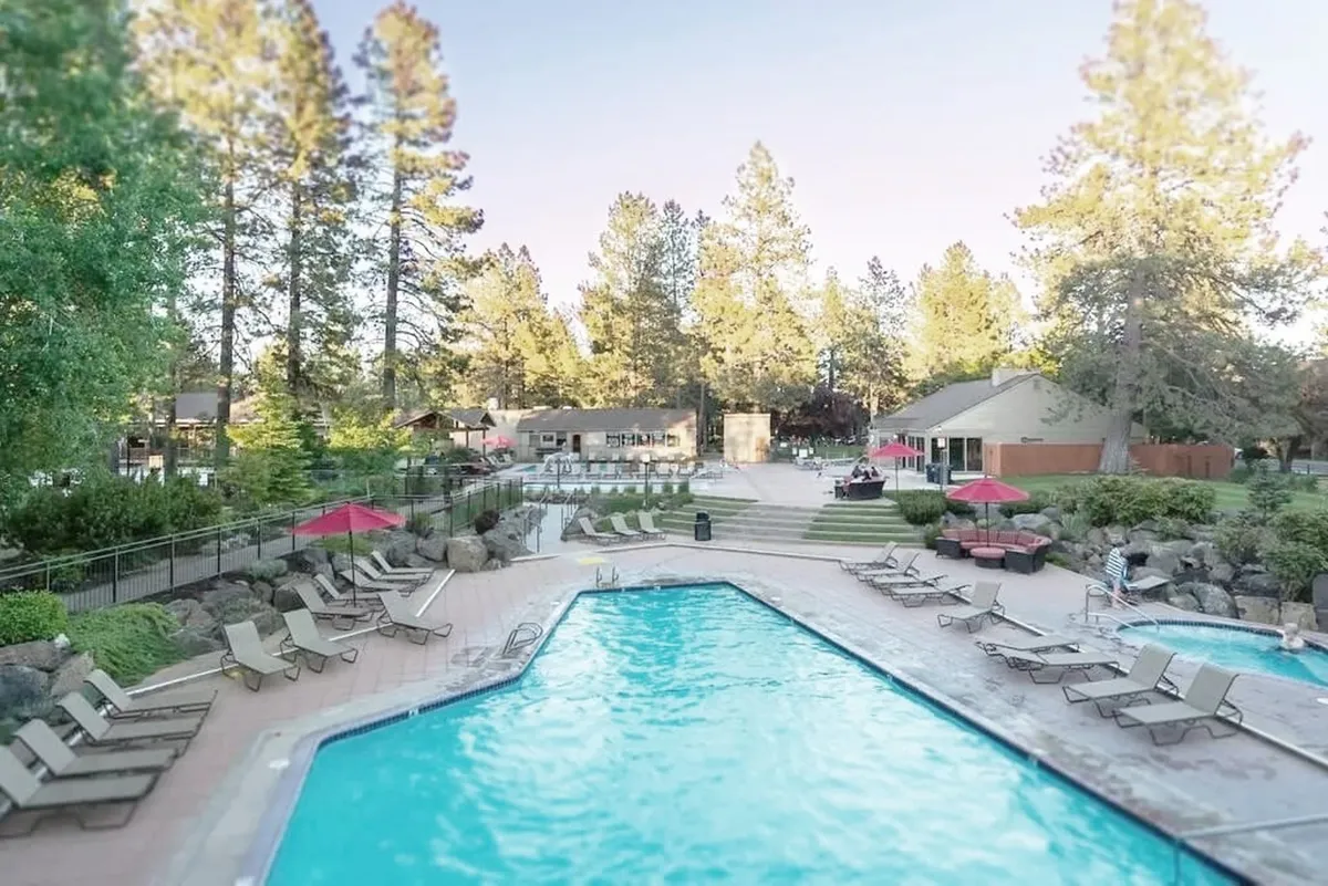 This image features the resort's inviting outdoor swimming pool, surrounded by lounge chairs and mature trees. The recreational area is open and landscaped, offering a welcoming space for guests to relax and socialize. The natural setting hints at the proximity to nature trails and outdoor amenities, aligning with the section's emphasis on outdoor exploration and pet-friendly adventure.